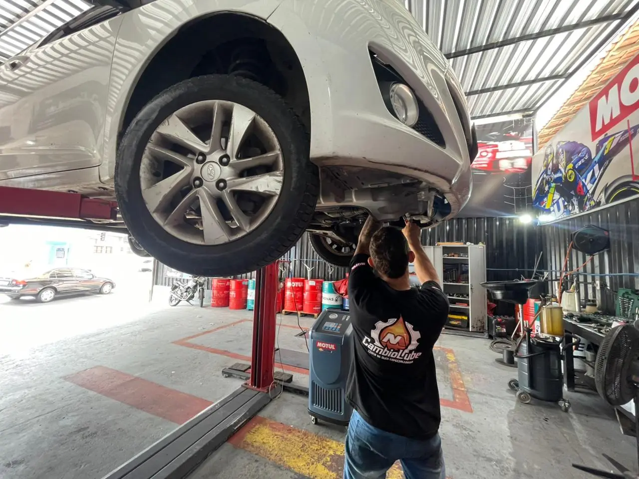 Mecânico trabalhando embaixo do carro no elevador, soltando o cárter do câmbio